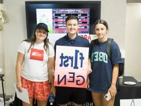 Three students stand together and smile at the camera while holding a sign