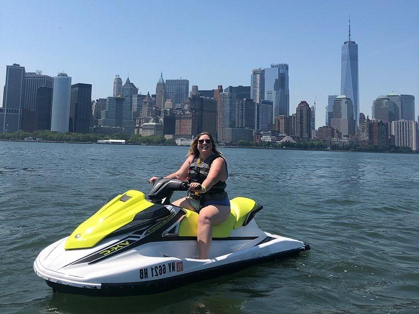 Milly Treu riding a jet ski with the New York City skyline in the background.